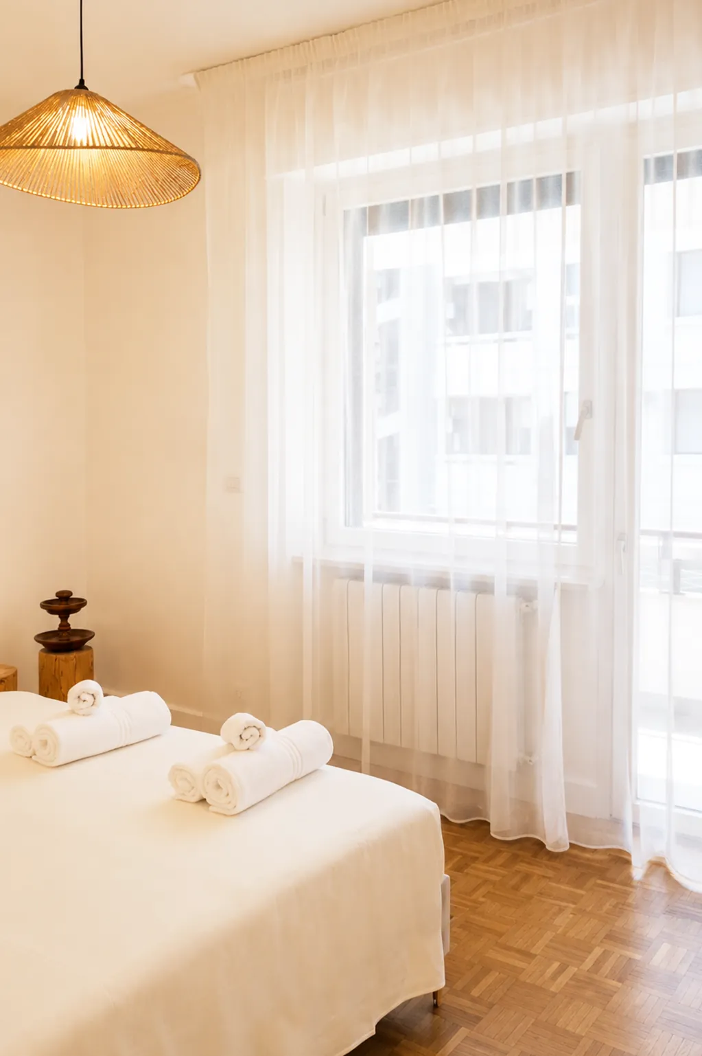 Finestra con tende chiare e lampadario in fibra sopra il letto