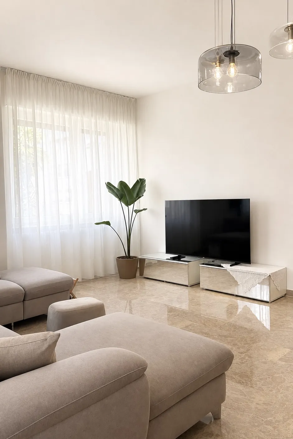 Soggiorno con divano angolare grigio, televisore e una pianta vicino alla finestra